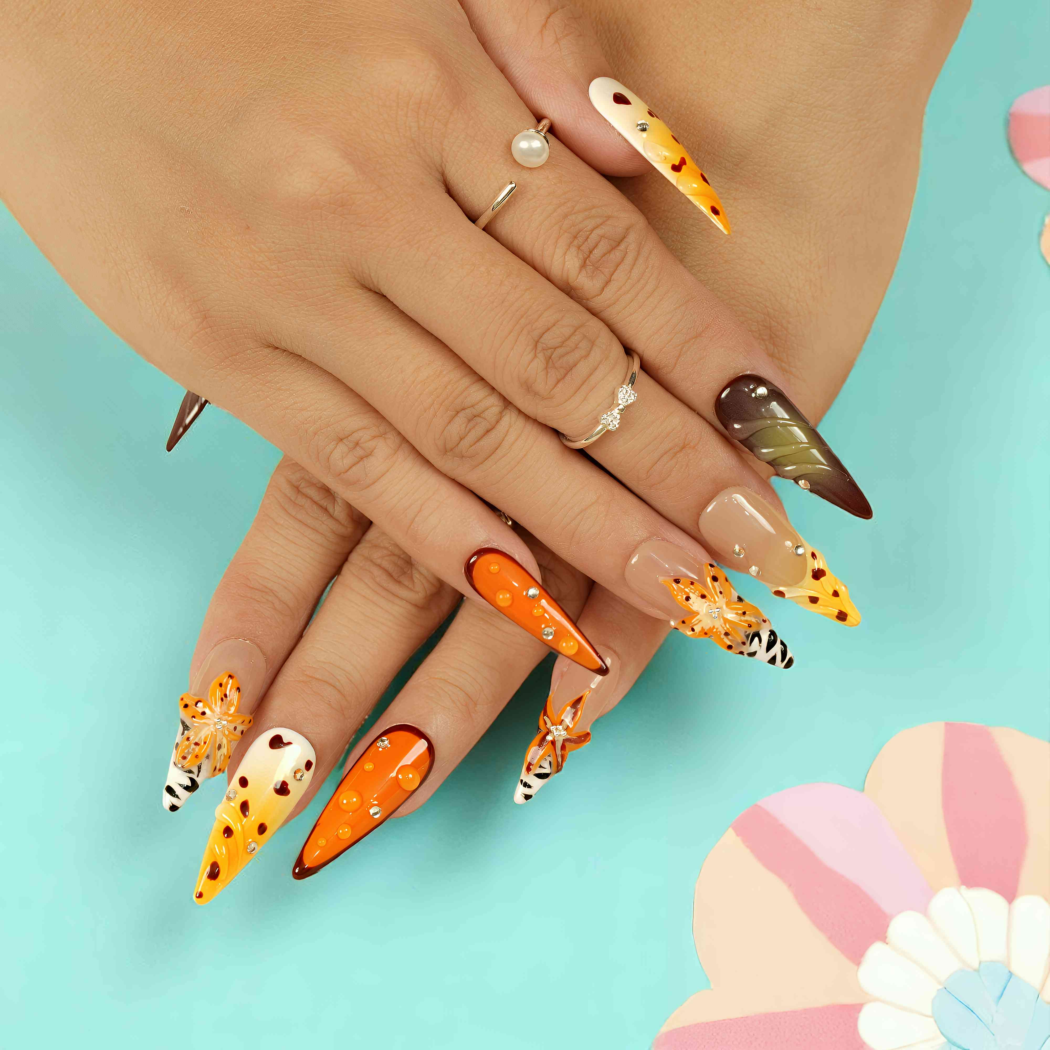 Hand with long almond-shaped press on nails in a leopard and floral design, featuring orange, white, and brown tones on a pastel background